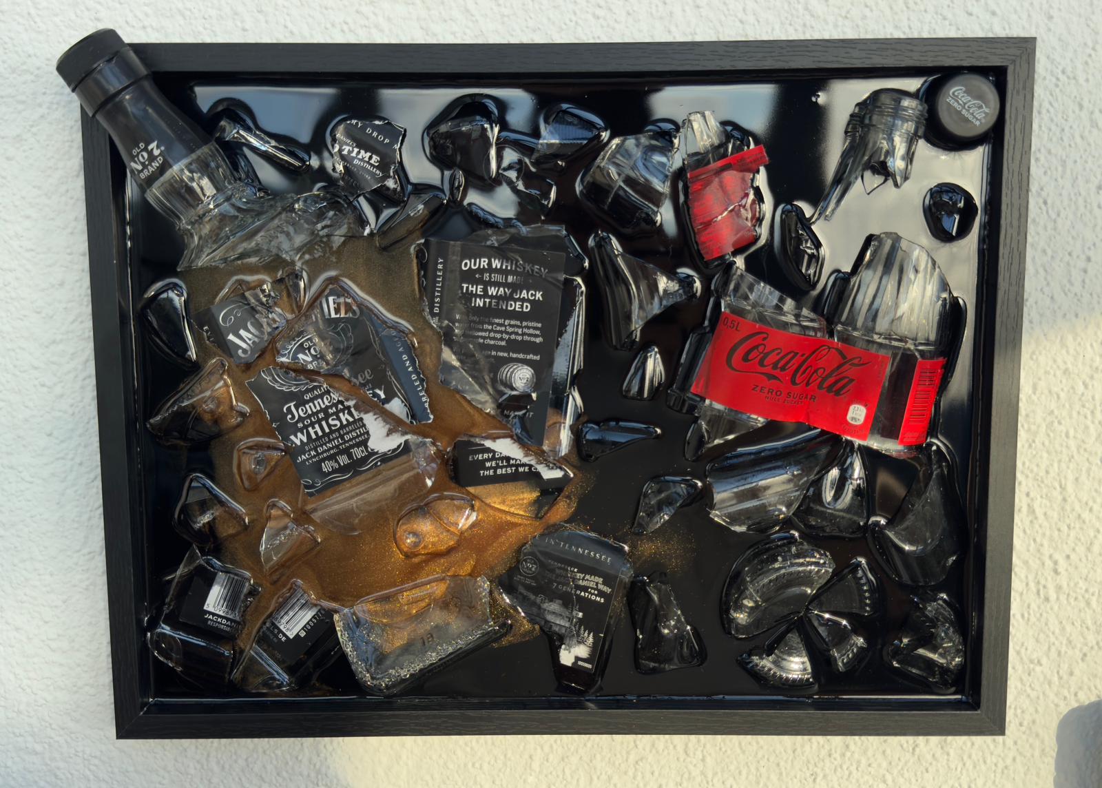 Gerahmtes 3D-Upcycling-Kunstwerk aus zerbrochenen Glasflaschen von Jack Daniel’s Whiskey und Coca-Cola Zero, arrangiert auf schwarzem Hintergrund mit sichtbarer Whiskey-Färbung und Glasfragmenten.