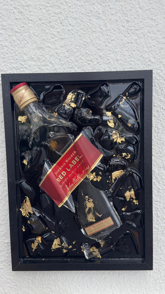 „Gerahmtes Mixed-Media-Kunstwerk mit zerschlagener Johnnie-Walker-Red-Label-Whiskyflasche auf schwarzem Hochglanz-Hintergrund, veredelt mit goldenen Blattgold-Akzenten.“